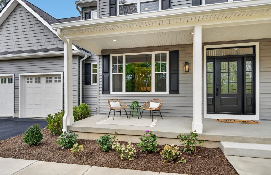 Covered front porch of a home with gray siding and landscaped garden beds