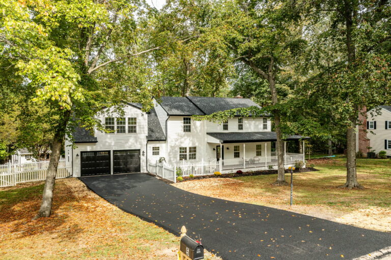 Aerial view of a white two-story home with a long driveway on a wooded lot