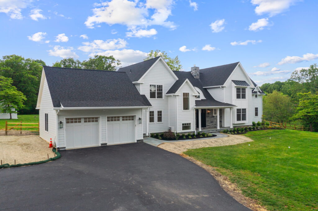 White two-story home with a two-car garage and green lawn under a blue sky